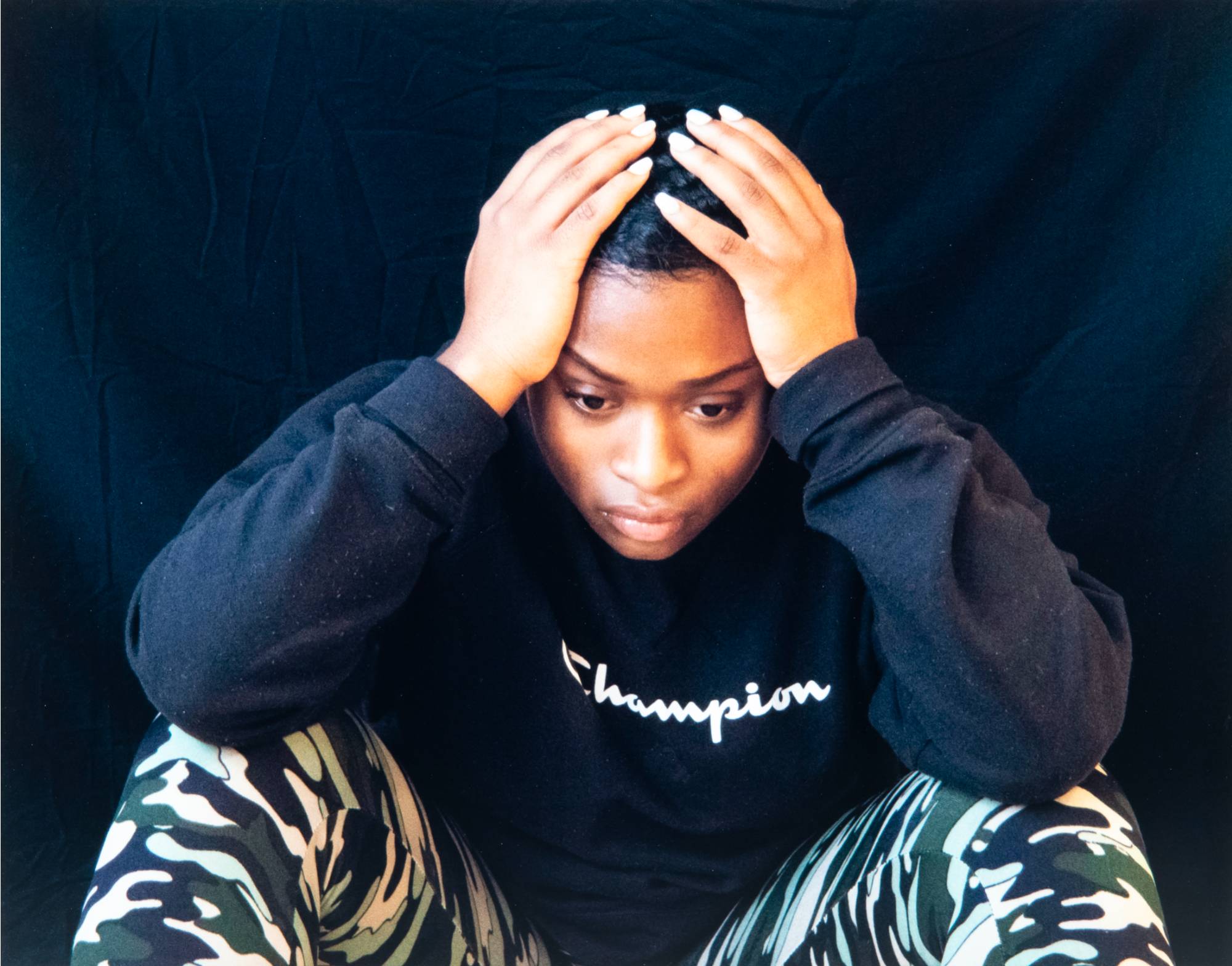 Image of a person hunched over their knees, head in their hands.